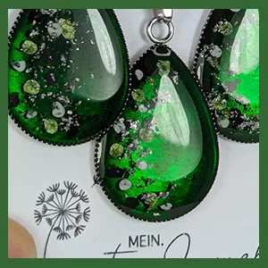 Grüne tropfenförmige Ohrringe und Halskette mit eingebetteten getrockneten Blüten und Glitzerpartikeln.